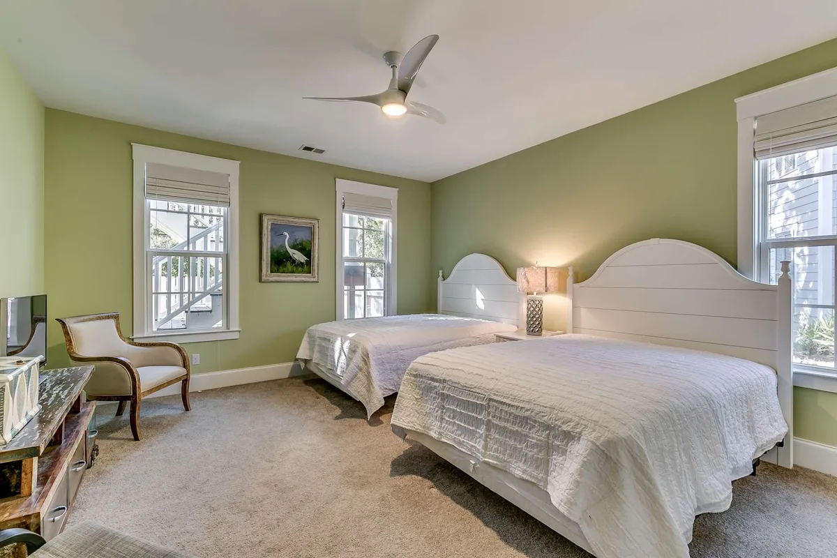 A cozy guest room with two beds, a decorative lamp, framed artwork, and large windows letting in ample sunlight. The atmosphere is serene, ideal for relaxation or intimate conversations. This space is well-suited for families or groups, mirroring the section's double-queen guest room feature.