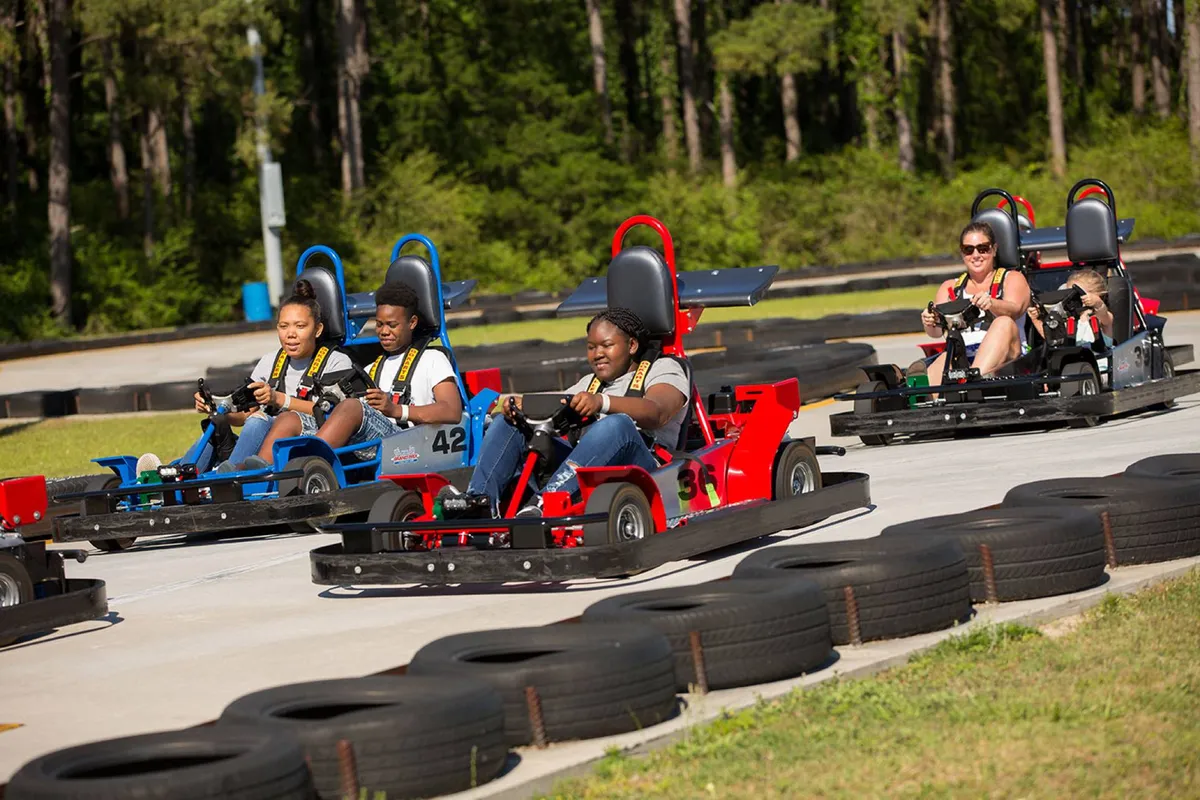 A lively go-kart racing track bustling with participants, colorful karts, and cheering onlookers. The atmosphere is energetic and playful, capturing the thrill and excitement of family outings or group competitions. The track is surrounded by tires, adding to the sense of action and fun.