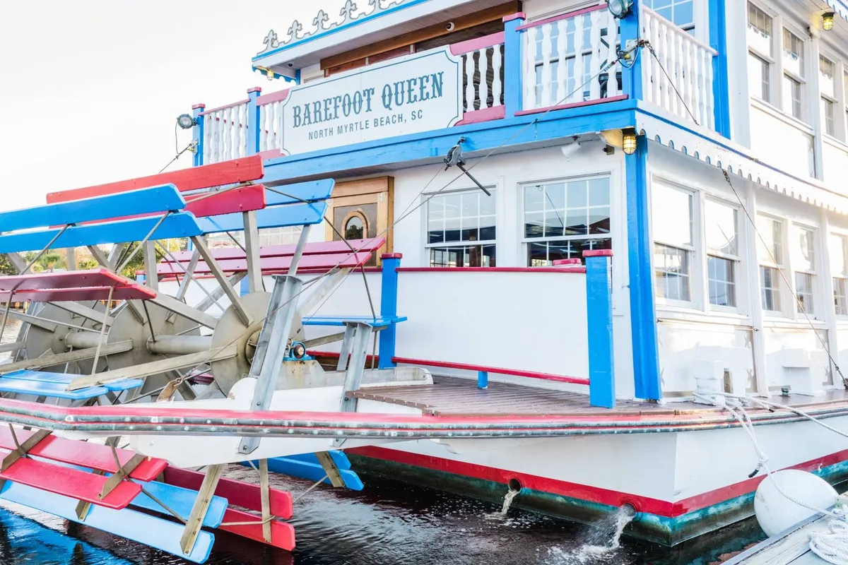 This vibrant exterior scene shows a paddle wheel, colorful building facade, and visible signage, hinting at lively dining, entertainment, and sightseeing options. The festive mood aligns with exploring local attractions beyond the golf course.