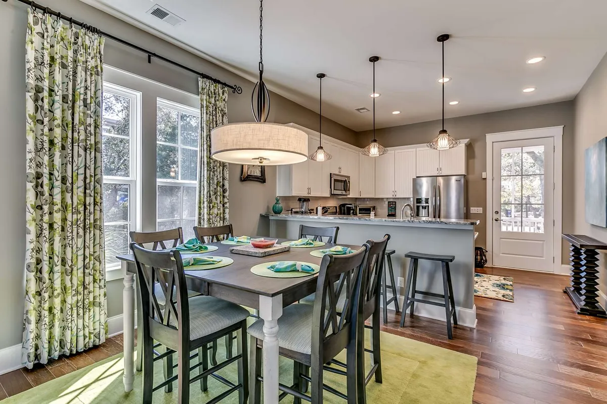 A warm, inviting dining area with a large table, decorative curtains, and a kitchen island in the background. The space is designed for family meals, friendly conversations, and celebratory gatherings.