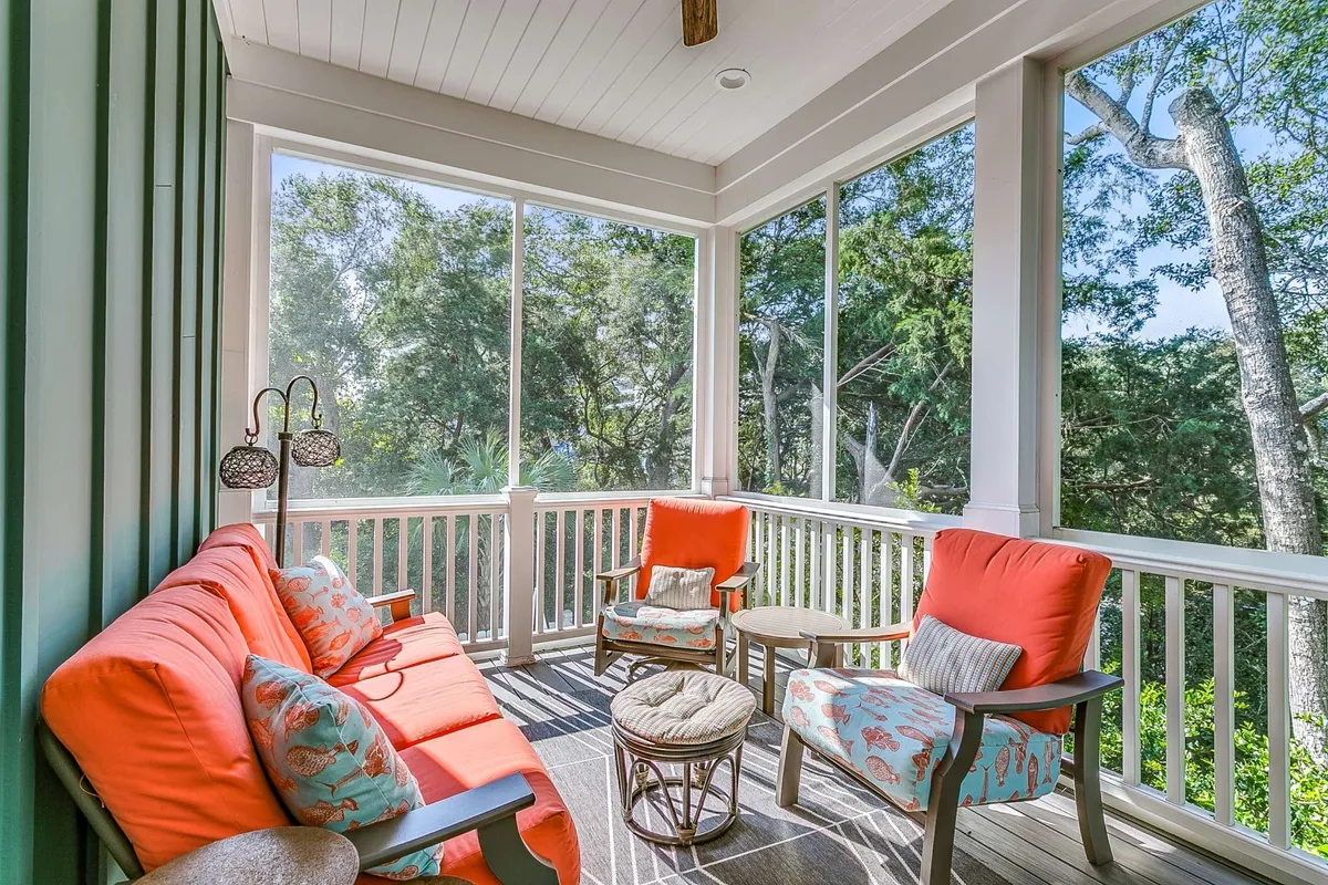 A tranquil screened porch with comfortable seating, decorative pillows, and large screened windows framing views of the outdoors. The space feels airy and inviting, ideal for morning coffee or unwinding after a swim.
