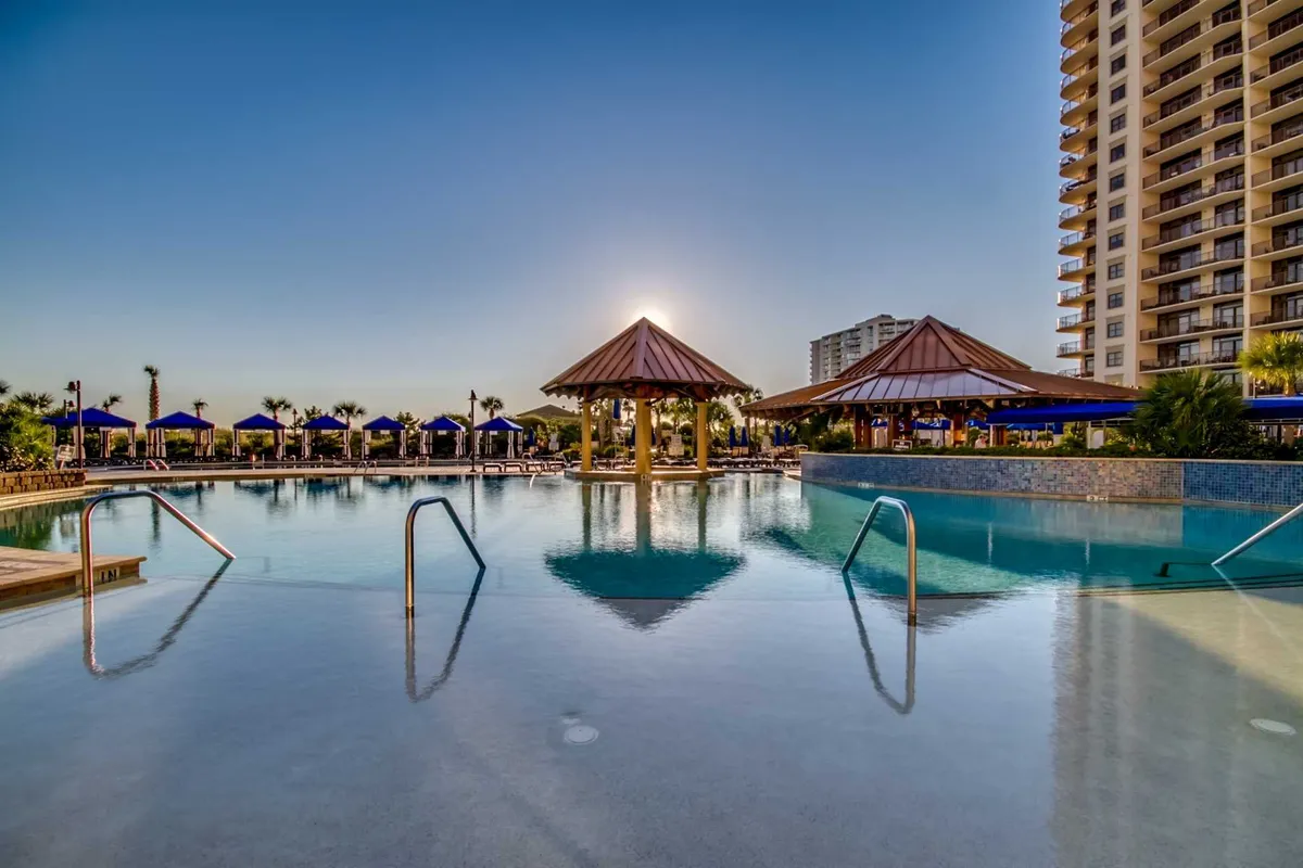 An inviting outdoor pool area surrounded by palm trees, lounge chairs, and shaded pavilions. The scene exudes a tranquil and leisurely vibe, with plenty of space for guests to swim, sunbathe, or gather for poolside fun. The environment suggests both relaxation and group enjoyment, perfect for multi-generational gatherings.