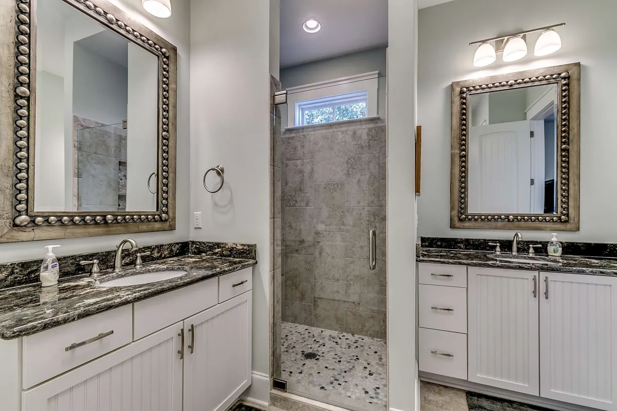 A modern bathroom featuring large mirrors, a granite countertop, and a sleek shower. The space is serene and bright, ideal for self-care and providing ample room for guests to refresh and unwind after a long day.